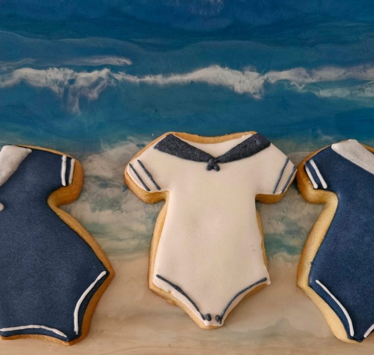 Biscuits décorés naissance bébé Trois biscuits en forme de maillots de bain sur fond marin.