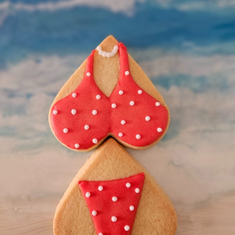 Bikini rouge biscuits décorés Un biscuit en forme de maillot de bain rouge à pois blancs sur fond de plage.