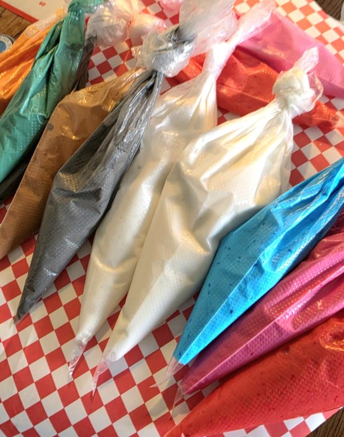 biscuits décorés Sacs de glaçage en différentes couleurs sur un napperon à carreaux rouges et blancs.